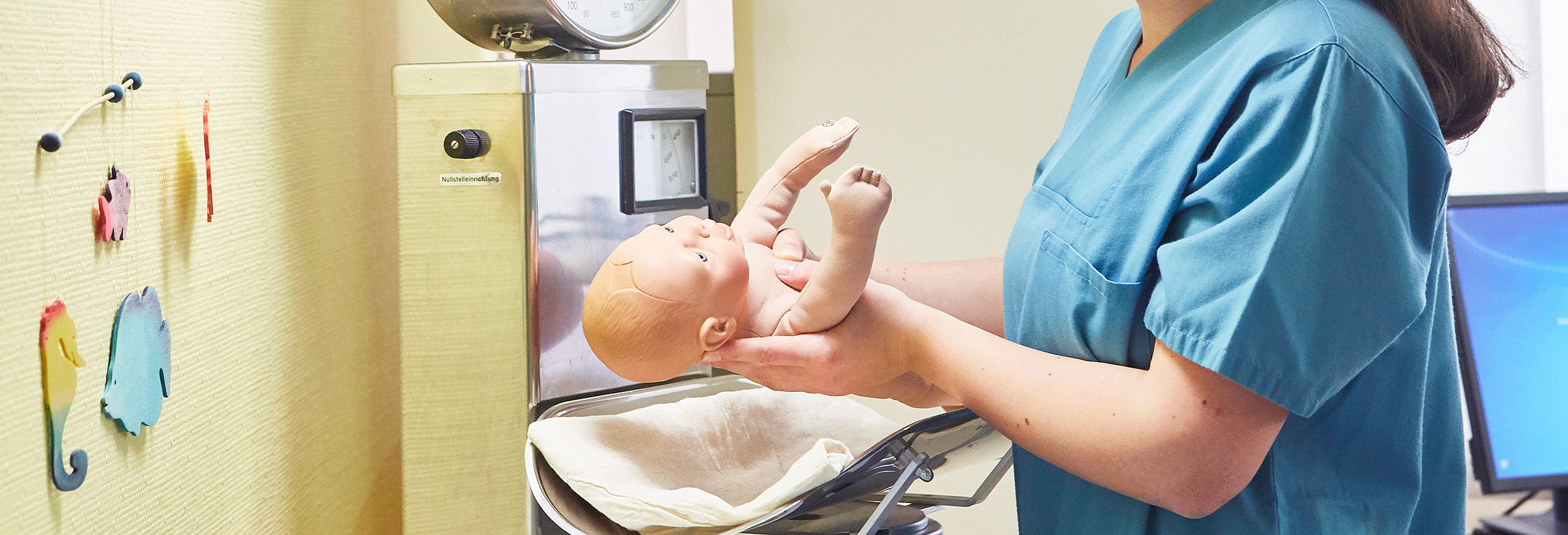 Hebamme in Ausbildung legt Babypuppe auf die Waage